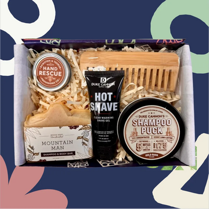 Grooming kit with Duke Cannon products including a shampoo puck, hot shave gel, and mountain man soap on a colorful background.