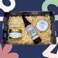 Gift set with lip butter, spray, and honey in a decorative box against a colorful abstract background.