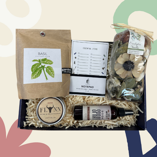 A gift box containing various home essentials such as a notepad, coffee rub, garden in a bag with basil, room and linen spray, and clean cotton.