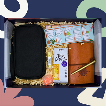 Gift box with black travel case, brown leather journal, Twin Engine coffee, and other items on a colorful background