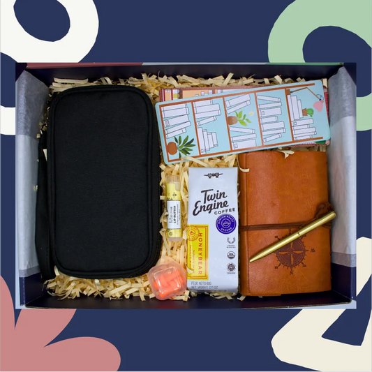 Gift box with black travel case, brown leather journal, Twin Engine coffee, and other items on a colorful background