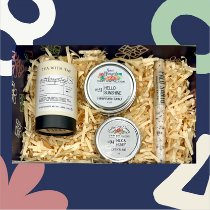 Gift set with 'Tea with Tea' product, 'Hello Sunshine' candle, 'Honey' lotion bar, and a small tube of cream on shredded paper.