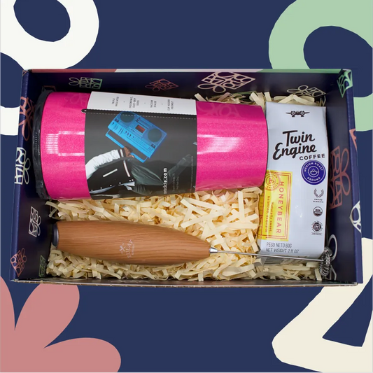 Gift box with pink mug, coffee package, and wooden item on a colorful background